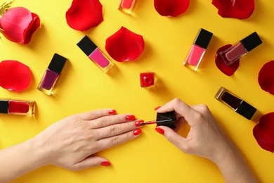 Woman applying bright nail polish on color background, top view