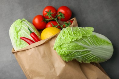 Paper bag with fresh Chinese cabbages, lemon, tomatoes and chili pepper on grey textured table, flat lay