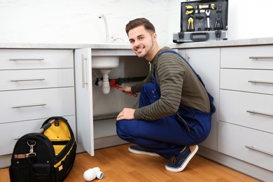 Photo of Male plumber in uniform repairing kitchen sink