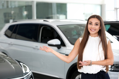 Young saleswoman standing in modern car salon