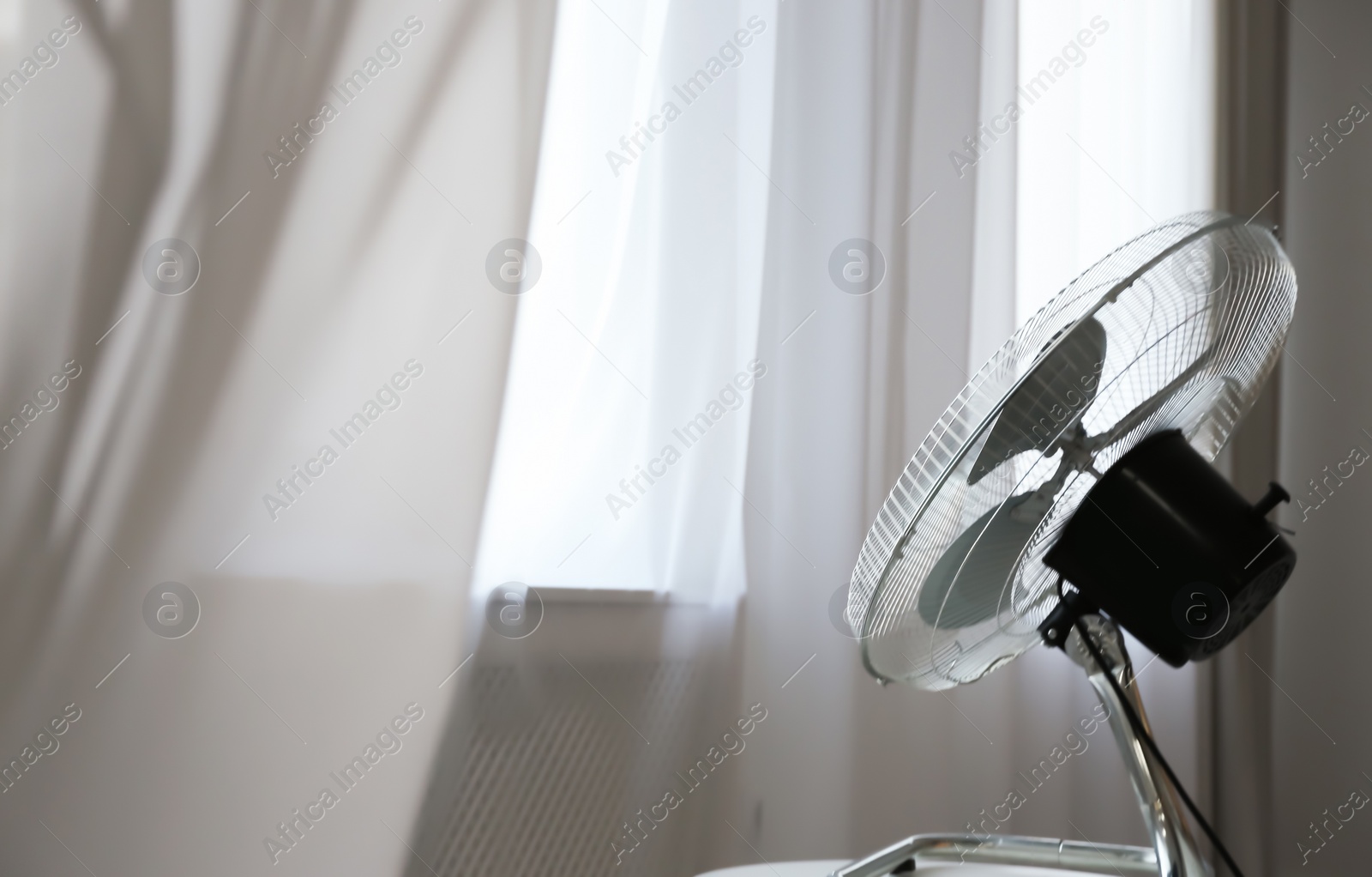 Photo of Modern electric fan on white table near window indoors. Space for text