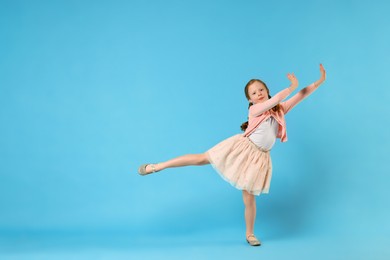 Photo of Cute little girl dancing on light blue background, space for text