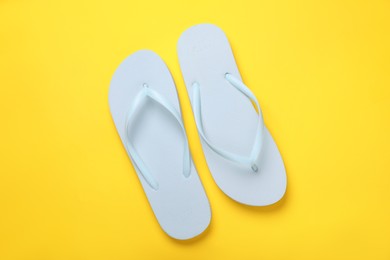 Stylish white flip flops on yellow background, top view