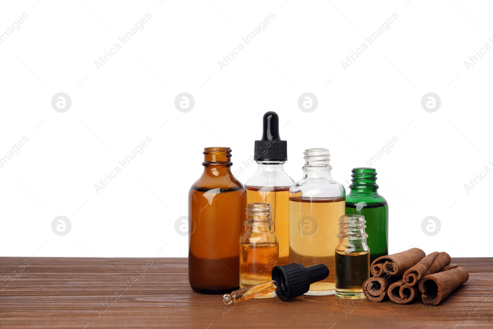 Photo of Bottles of essential oils and cinnamon sticks on wooden table against white background