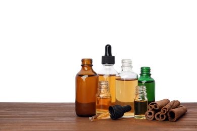 Photo of Bottles of essential oils and cinnamon sticks on wooden table against white background