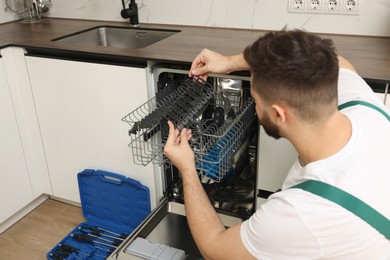 Photo of Serviceman examining dishwasher cutlery rack in kitchen