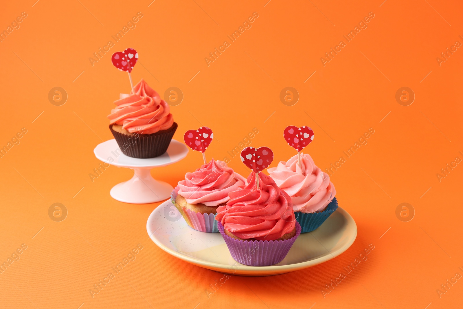 Photo of Delicious cupcakes with bright cream and heart toppers on orange background