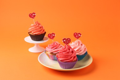 Delicious cupcakes with bright cream and heart toppers on orange background