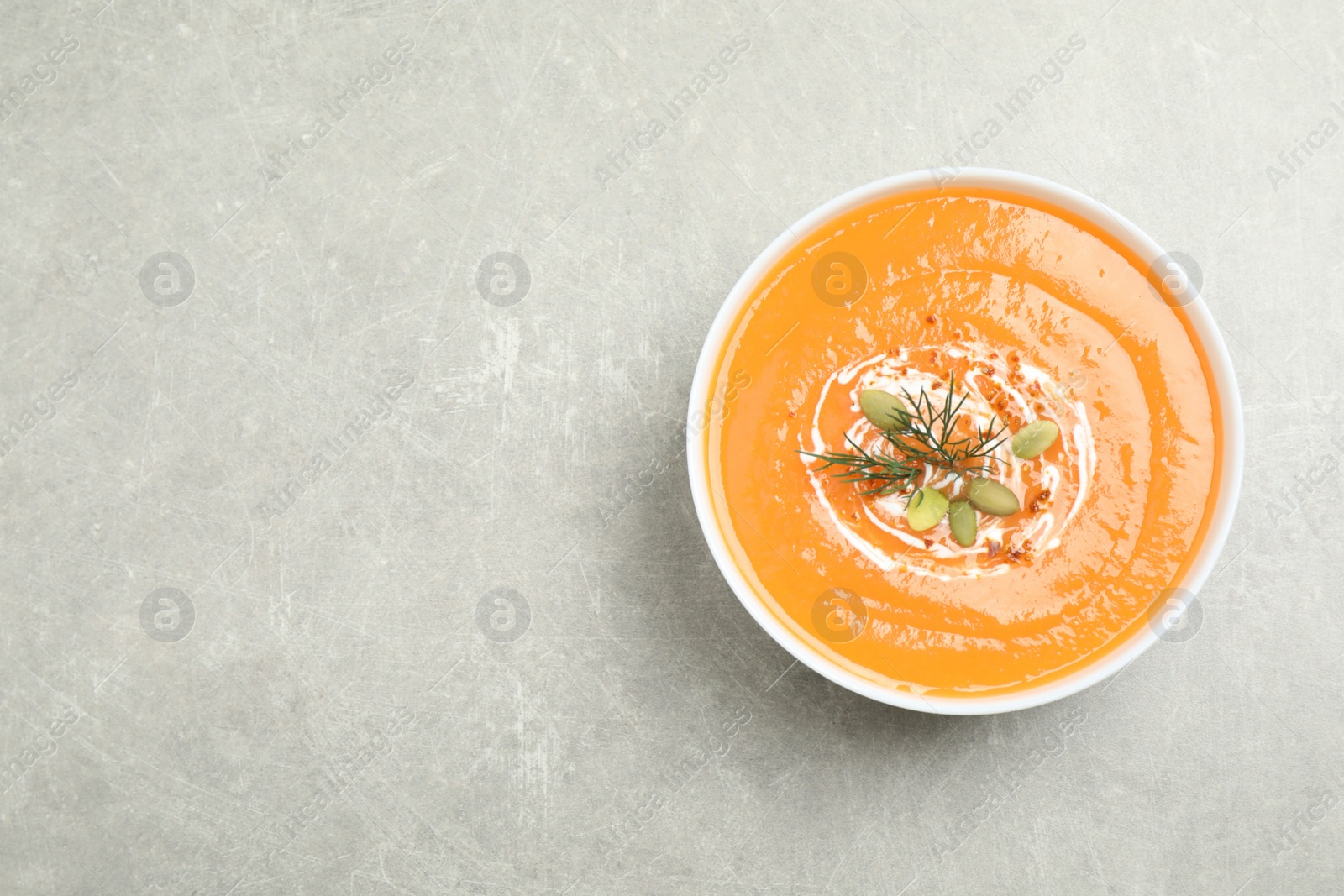 Photo of Delicious pumpkin soup in bowl on grey table, top view. Space for text