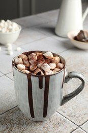 Photo of Delicious hot chocolate with marshmallows and cocoa powder in cup on tiled table