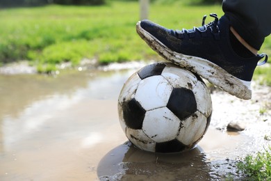Photo of Man with dirty soccer ball near puddle outdoors, closeup
