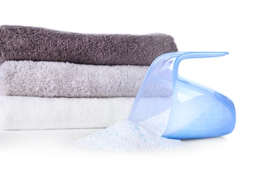 Laundry detergent in plastic measuring cup and towels on white background