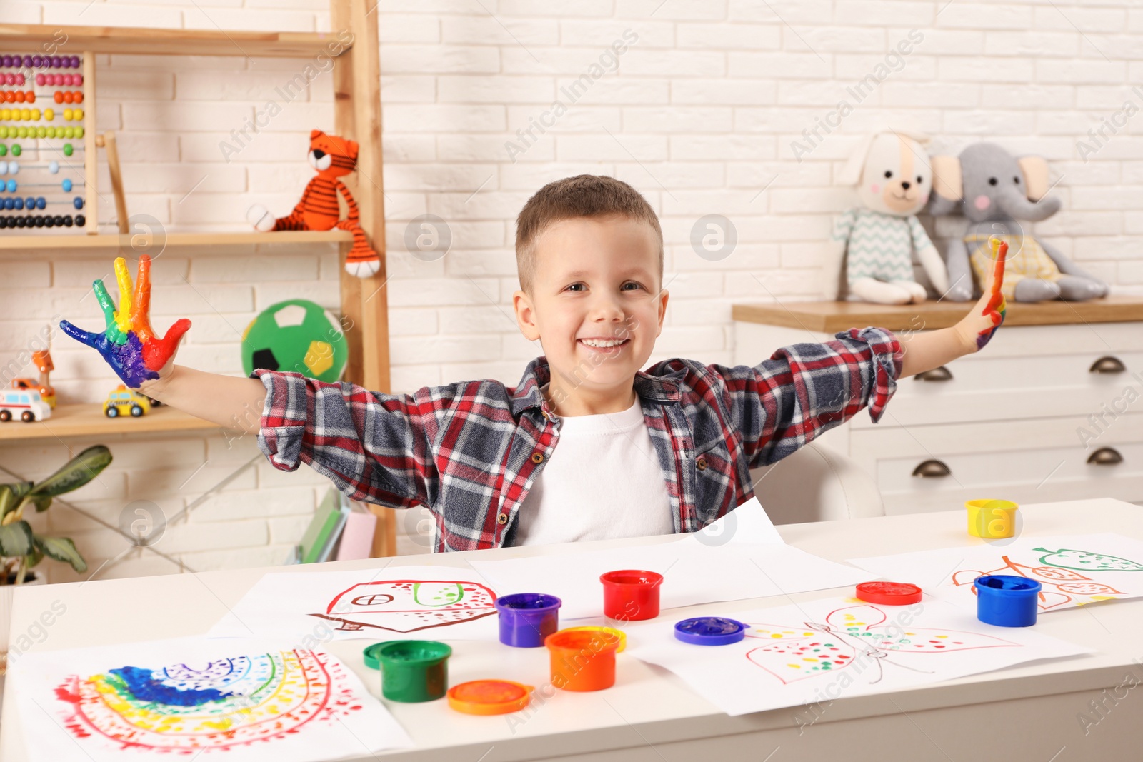 Photo of Happy little boy showing painted palms at white table in room