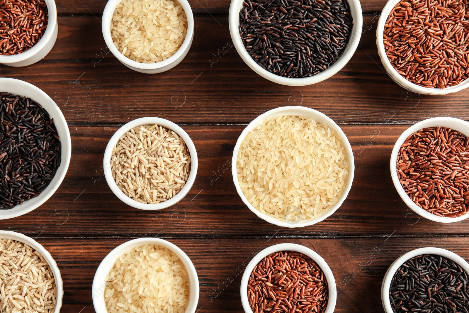 Photo of Bowls with different types of rice on wooden background, top view