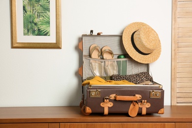 Photo of Vintage suitcase with clothes and shoes on chest of drawers indoors
