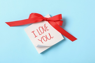 Memory stickers with text I Love You and red bow on light blue background, top view