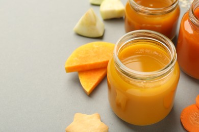 Photo of Jars with healthy baby food, pumpkin, apple and cookie on grey background, closeup. Space for text