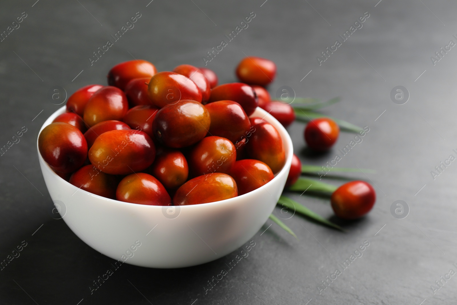 Photo of Palm oil fruits in bowl on black table, closeup
