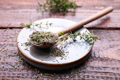 Photo of Spoon with dried thyme and fresh twigs on wooden table