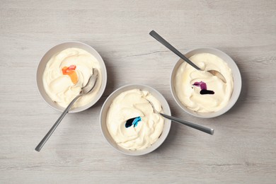 Bowls of different cream with food coloring on white wooden table, flat lay