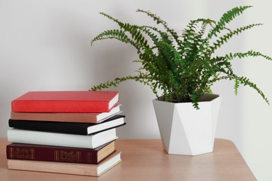 Stack of different hardcover books and beautiful houseplant on wooden table indoors