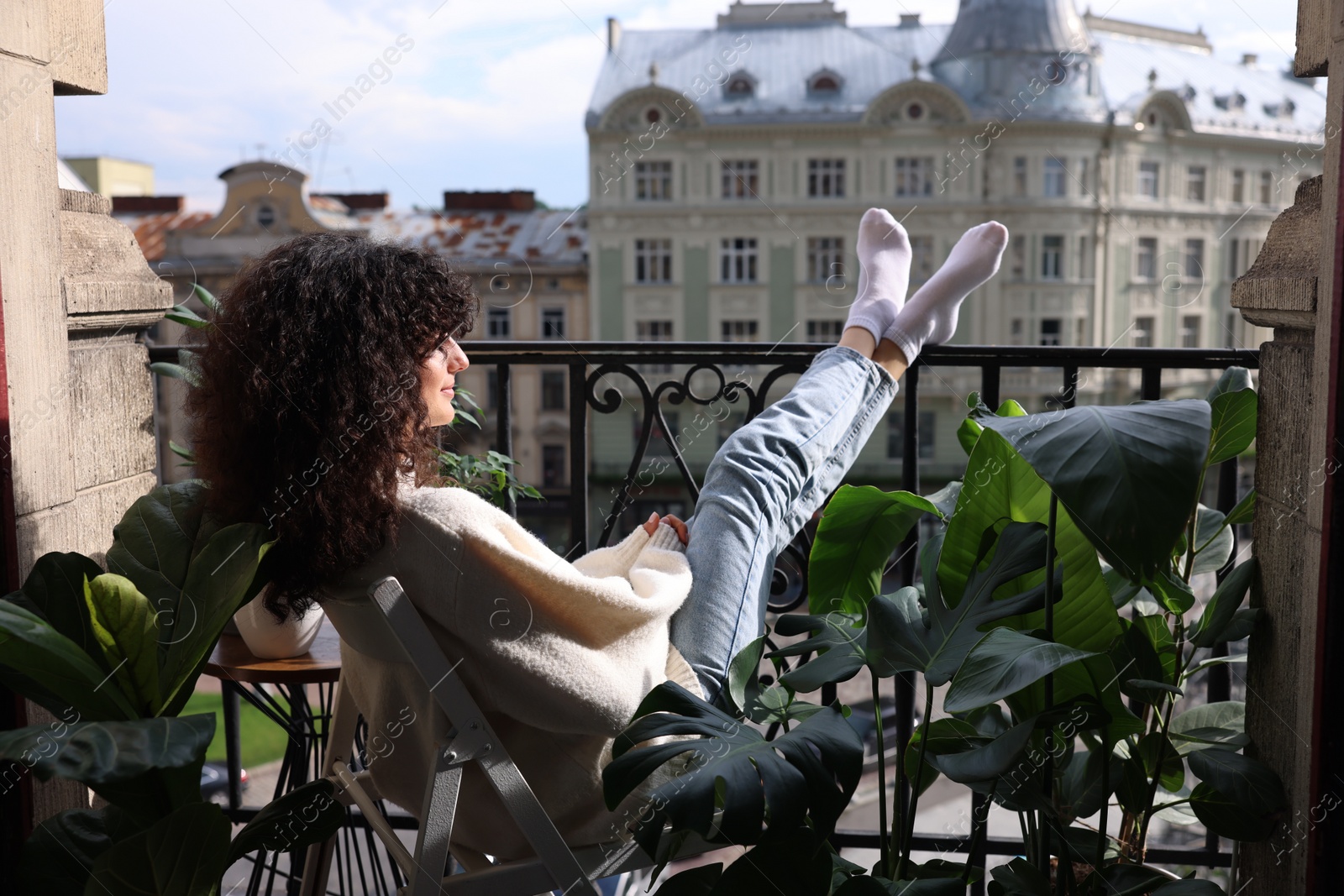 Photo of Beautiful young woman relaxing in chair surrounded by green houseplants on balcony