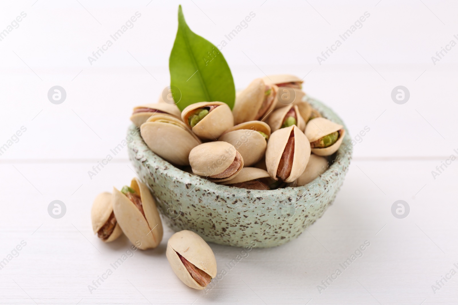 Photo of Delicious pistachios in bowl on white table