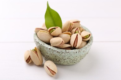 Delicious pistachios in bowl on white table