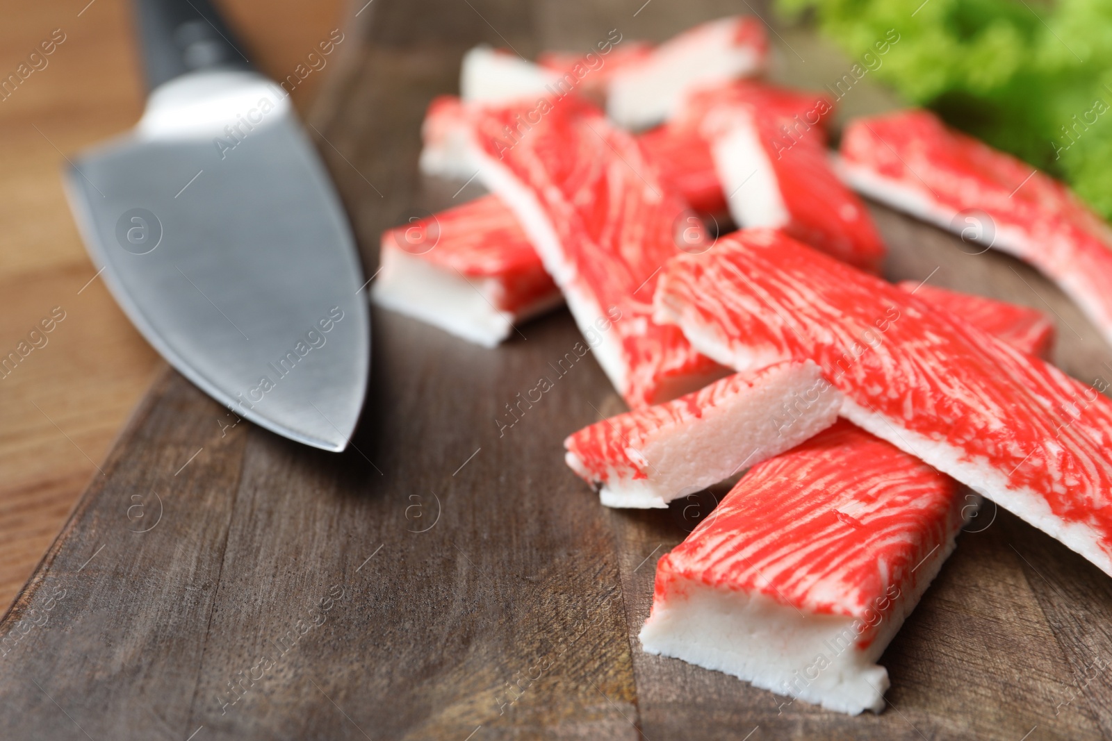 Photo of Delicious crab sticks with knife on wooden table, closeup