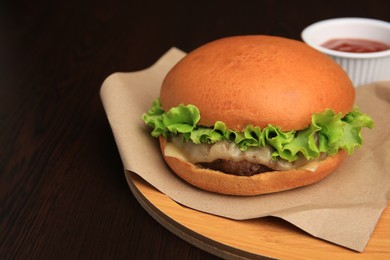 Board with tasty cheeseburger and sauce on wooden table, closeup. Space for text