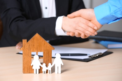 Photo of Man shaking hands with real estate agent at table, focus on family and house figures. Home insurance