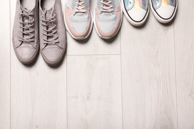 Photo of Different sneakers on wooden floor, top view with space for text