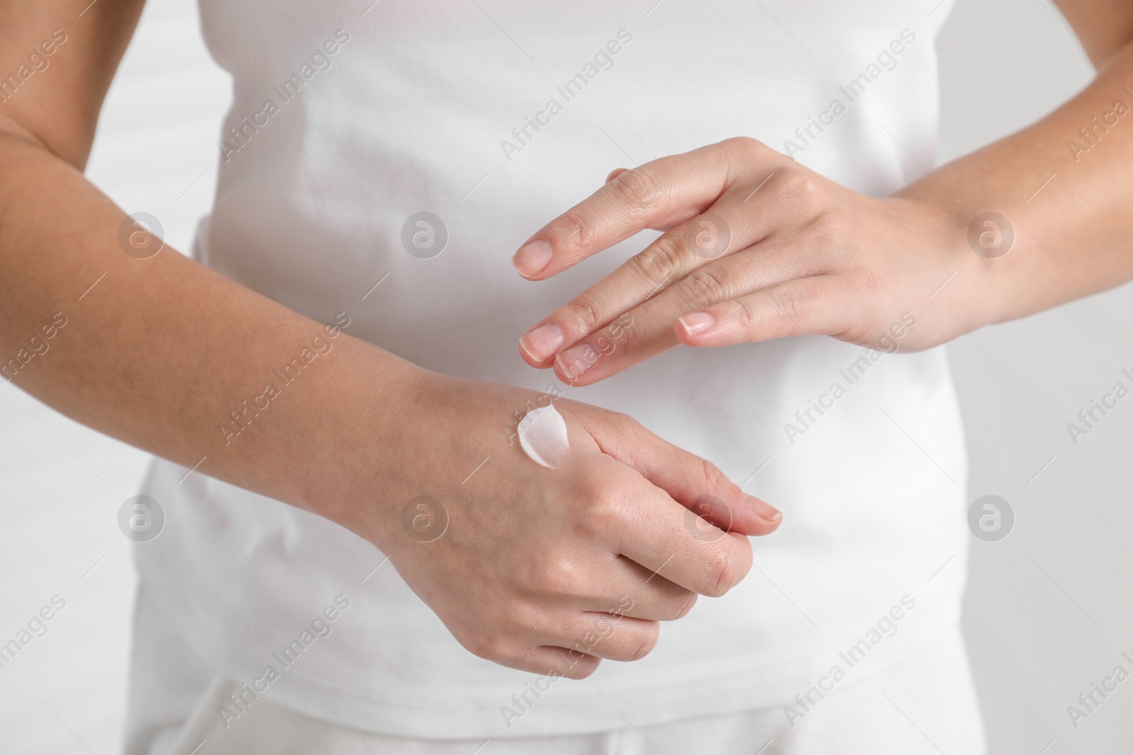 Photo of Woman applying cosmetic cream onto hand on blurred background, closeup