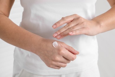 Photo of Woman applying cosmetic cream onto hand on blurred background, closeup