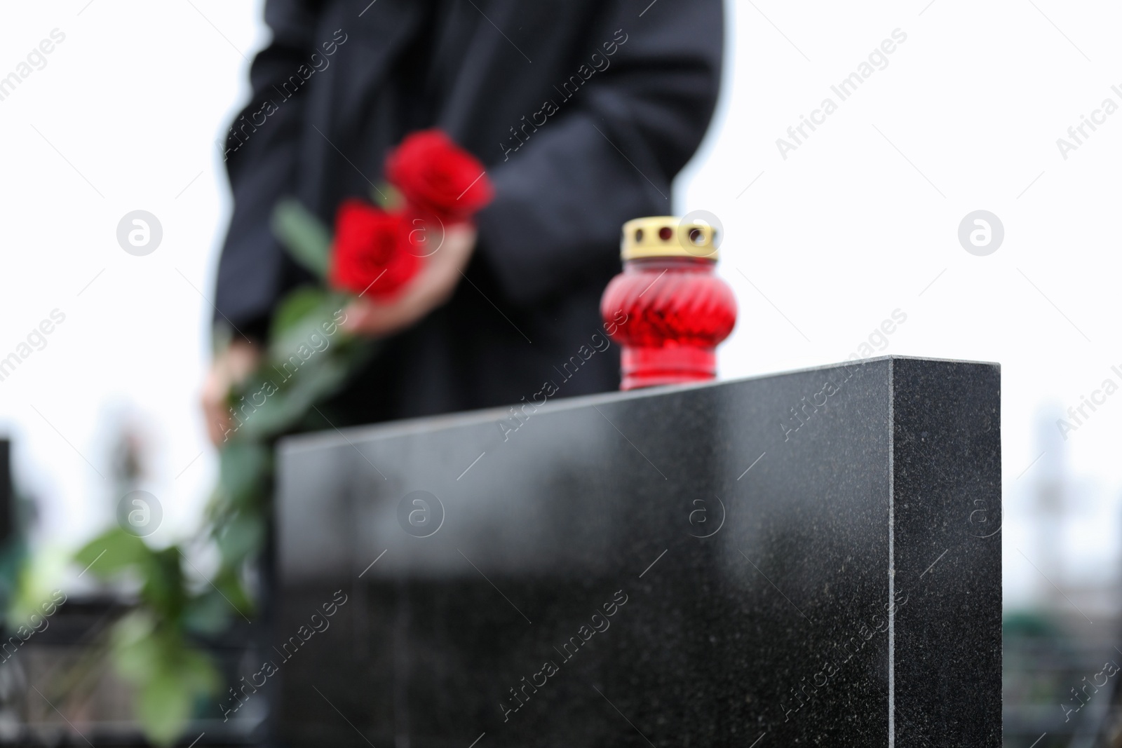 Photo of Woman with red roses outdoors, focus on candle. Funeral ceremony