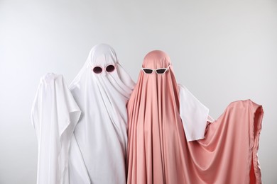 Photo of Glamorous ghosts. Women in color sheets with sunglasses on light grey background