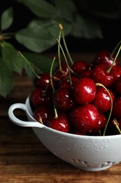 Wet red cherries in colander on wooden table