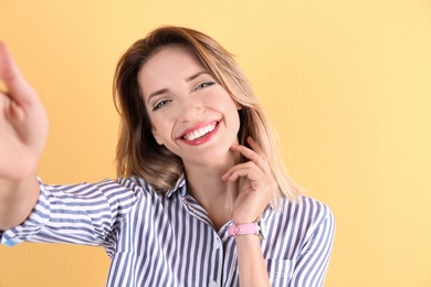 Beautiful laughing woman taking selfie on color background