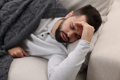 Photo of Man suffering from headache on sofa under blanket