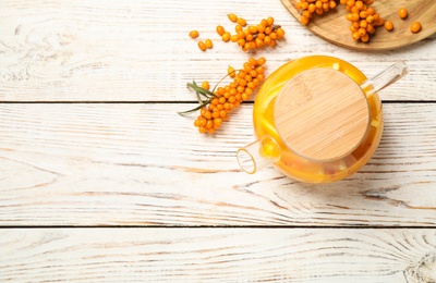 Photo of Delicious sea buckthorn tea with orange slices and fresh berries on white wooden table, flat lay. Space for text