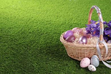Photo of Easter basket with painted eggs and iris flowers on green grass. Space for text