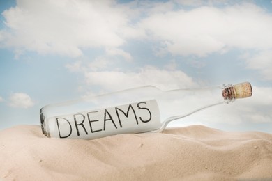 Photo of Corked glass bottle with Dreams note on sand against sky