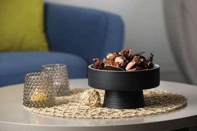 Photo of Aromatic potpourri of dried flowers and burning candles on table indoors
