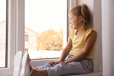 Photo of Portrait of cute little girl on window sill at home