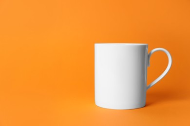 Photo of One white ceramic mug on orange background. Space for text