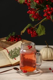 Photo of Delicious viburnum tea, book and pumpkin on wooden table against dark background. Cozy autumn atmosphere