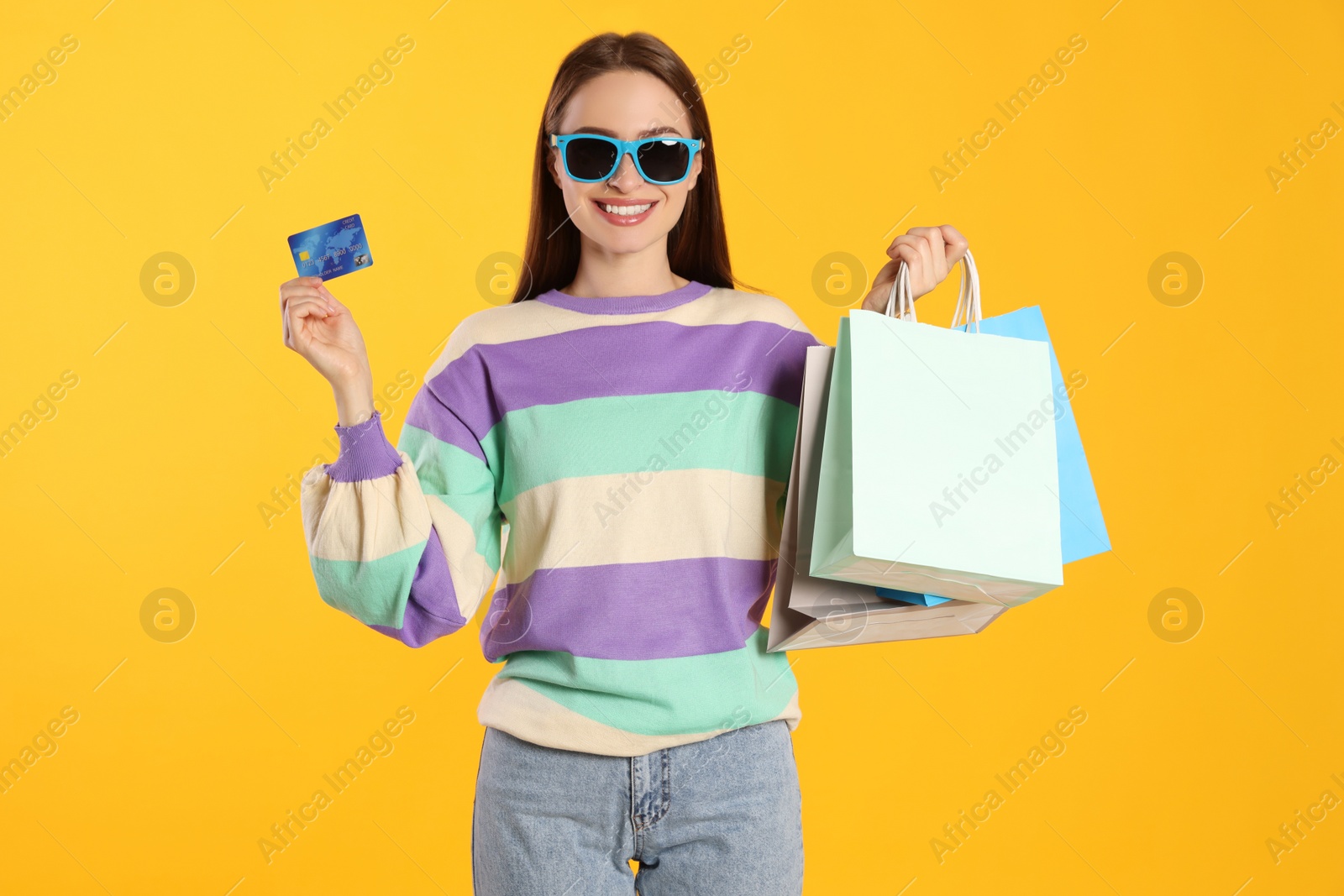 Photo of Happy young woman with shopping bags and credit card on yellow background. Big sale