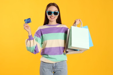 Happy young woman with shopping bags and credit card on yellow background. Big sale