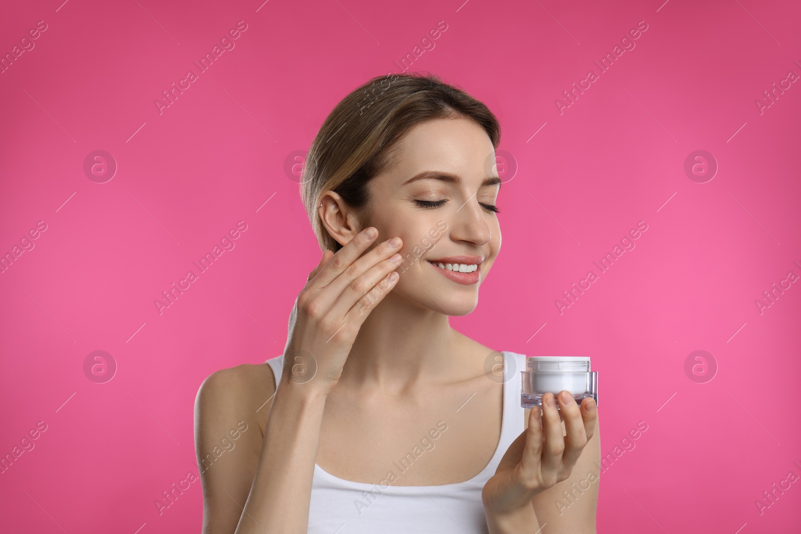 Photo of Young woman applying facial cream on pink background