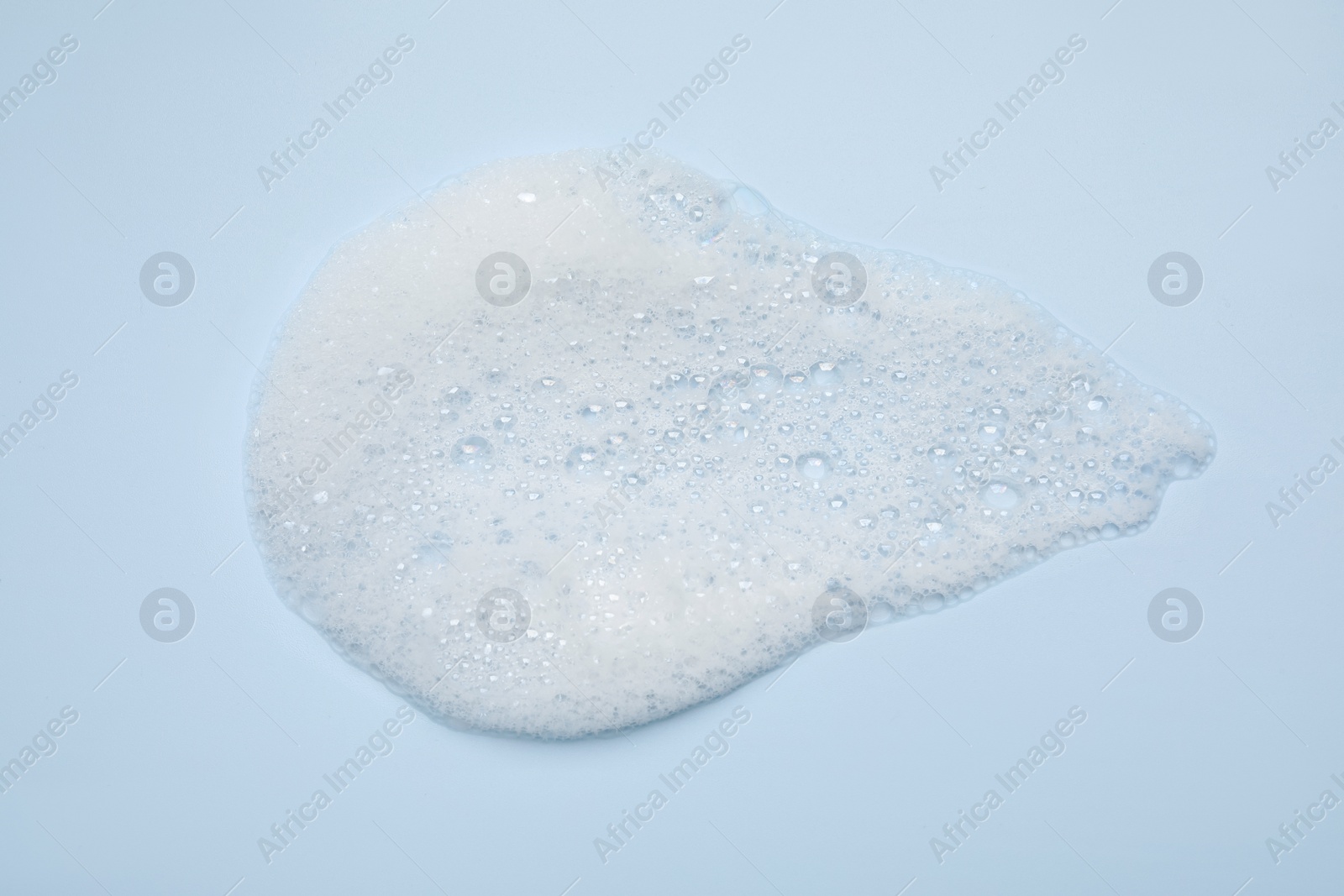 Photo of Spot of white washing foam on light blue background, top view